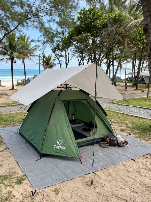 Equipamentos organizados para camping na praia com barraca montada em área estruturada próxima ao litoral.
