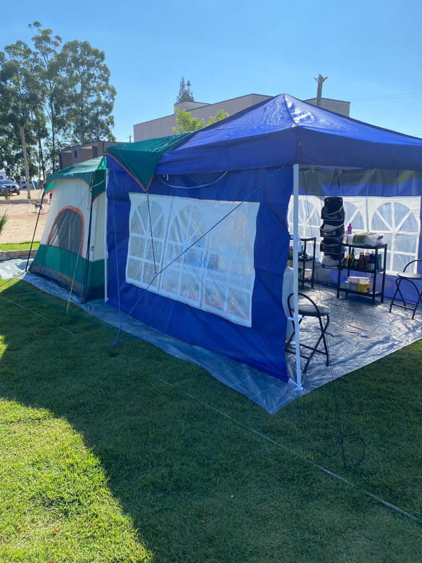 Por que usar uma ráfia de solo na estrutura de camping: barraca de camping e gazebo montados sobre uma ráfia de solo, com vários equipamentos de cozinha - visão lateral.